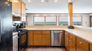 Una cocina moderna con armarios de madera, electrodomésticos de acero inoxidable y vistas al océano a través de amplios ventanales.