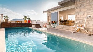 A swimming pool with a stone wall, outdoor seating, and a bar area.
