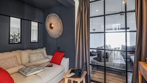A modern living room with a sofa, a laptop on a small table, and a large window with curtains.