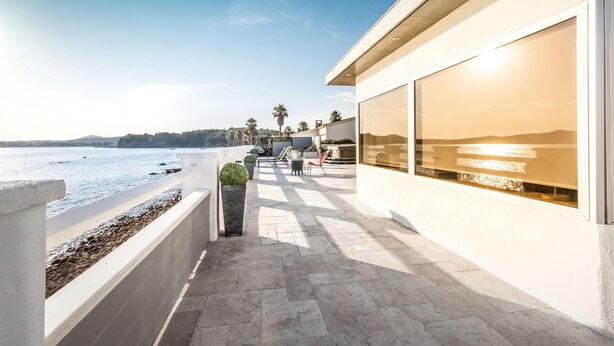 A modern building with large windows, a stone pathway, and a view of the sea.