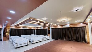 A spacious room with rows of white sofas arranged for seating, a stage area with curtains, and a modern ceiling design with recessed lighting. - HOTEL INDRALOK INN (Hazaribagh)