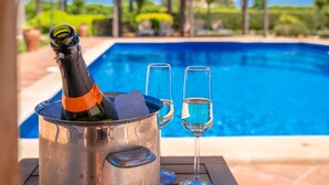 Une scène au bord de la piscine, avec une bouteille de champagne dans un seau en métal, deux coupes de champagne et une piscine à l’eau d’un bleu limpide.
