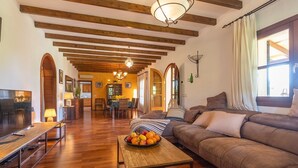 Un vaste espace de vie doté d’un plafond en bois, d’un canapé, d’une table à manger avec des chaises et d’un téléviseur.