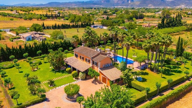 Une grande maison avec une piscine, entourée de jardins bien entretenus et de palmiers.