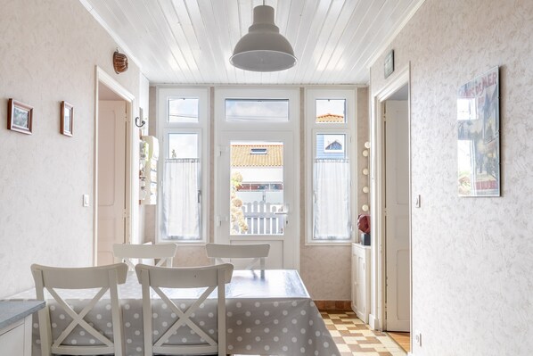 A dining area with a table and chairs, a ceiling light, and a view through the windows.