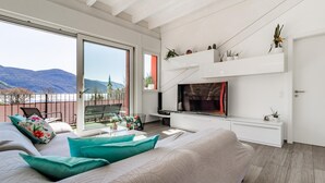 Un salon moderne doté d’un grand lit, d’une télévision et d’un balcon offrant une vue sur la montagne.