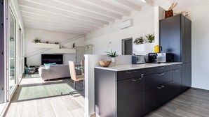 Une cuisine moderne avec des meubles de couleur sombre, un four à micro-ondes encastré et une machine à café. On y trouve également un coin repas avec un canapé et un téléviseur en arrière-plan.