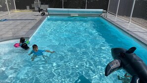 Une piscine à l’eau d’un bleu cristallin, un flotteur en forme de requin et un espace délimité par une clôture, équipé d’un accès pour fauteuils roulants.