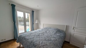 Une chambre à coucher avec un lit, une porte, une fenêtre avec des rideaux et une vue sur l’extérieur.