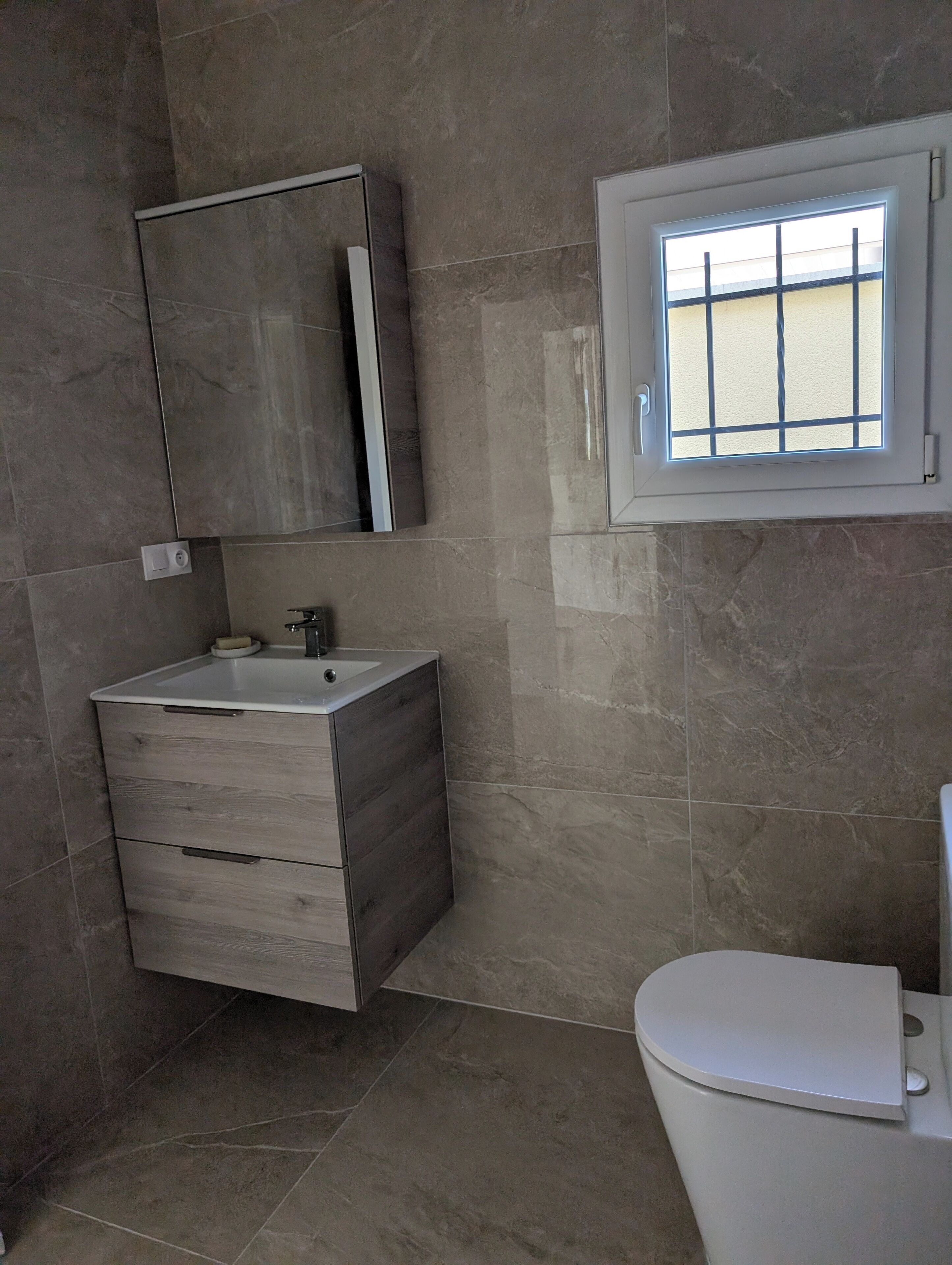 A bathroom with a modern design, featuring a wooden vanity, a mirror, a toilet, and a window with a grid pattern.
