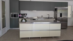 Une cuisine moderne avec des meubles gris, un îlot central en acier inoxydable, un four encastré et un réfrigérateur.
