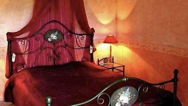 A bed with a red canopy, a small bedside table with a lamp, and a decorative mirror. - Dolce Vita (Mondragon)