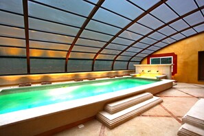An indoor swimming pool with a glass ceiling, a changing room, and a small window. - Dolce Vita (Mondragon)