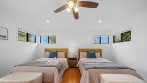 A hotel room with two beds, a ceiling fan, a nightstand with a lamp, and two windows with views of greenery. - @ Marbella Lane - Serene and Pristine Home (West Covina)