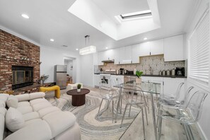 Un salon moderne avec une cheminée en briques, un canapé et une table à manger en verre, accompagnée de chaises.