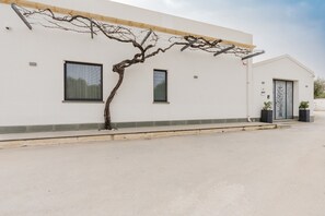 Un bâtiment moderne à la façade blanche, doté de deux fenêtres, d’une porte et d’un arbre qui pousse devant.