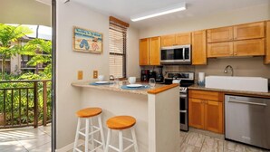 Una cocina con armarios de madera, microondas, lavaplatos y cafetera. Hay dos taburetes en la isla.