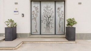 A building entrance with a modern door featuring a tree design, two potted plants, and a small sign on the wall. - Room 'Casa Umeli Giarraffa' with Shared Terrace, Wi-Fi and Air Conditioning (Marsala)