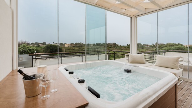 A hot tub with a view of the countryside, a wooden table with a bottle and glasses, and a cushioned seating area. - Room 'Casa Umeli Giarraffa' with Shared Terrace, Wi-Fi and Air Conditioning (Marsala)