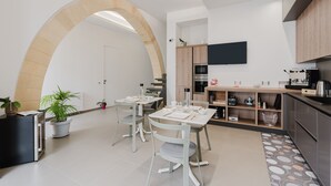 A modern kitchen with a dining area, a TV mounted above the counter, and a large arched doorway. - Room 'Casa Umeli Giarraffa' with Shared Terrace, Wi-Fi and Air Conditioning (Marsala)