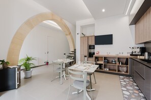 A modern kitchen with a dining area, a TV mounted above the counter, and a large arched doorway.