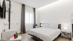 A modern hotel room with a large bed, bedside tables, a TV mounted on the wall, and a small seating area with a chair and a table. - Room 'Casa Umeli Giarraffa' with Shared Terrace, Wi-Fi and Air Conditioning (Marsala)