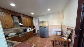 A compact kitchen with wooden cabinets, a stainless steel refrigerator, a microwave, and a dining table with chairs.