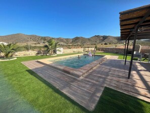Ein rechteckiger Swimmingpool mit Steinbord, umgeben von gepflegtem Rasen und einer Steinmauer.
