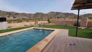 Une piscine bordée de pierres, une petite fontaine et une vue sur des collines en arrière-plan.