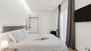 A modern hotel room with a bed, bedside table, lamp, and a flat-screen TV mounted on the wall.