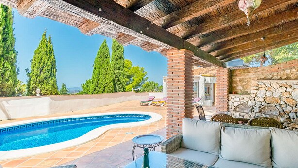 A poolside area with a curved pool, wicker furniture, and a stone wall. - Cruz del Monte in Cómpeta (Cómpeta)
