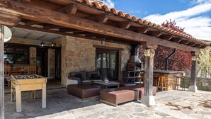 Un patio exterior con suelo de piedra, mobiliario de madera y una pared de piedra.