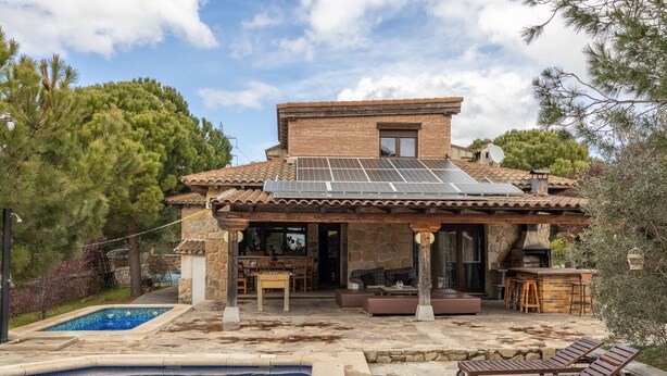 Una casa con piscina, mobiliario exterior y techo con paneles solares.