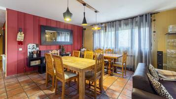 A dining area with wooden tables and chairs, a mirror on the wall, and a sofa with patterned cushions.
