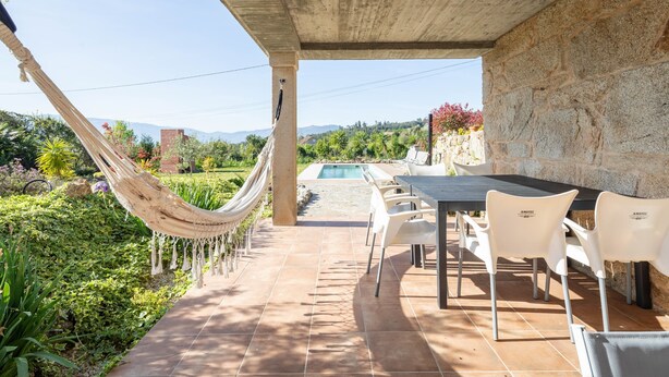 Une terrasse avec une table et des chaises, un hamac et une vue sur une piscine et des montagnes.