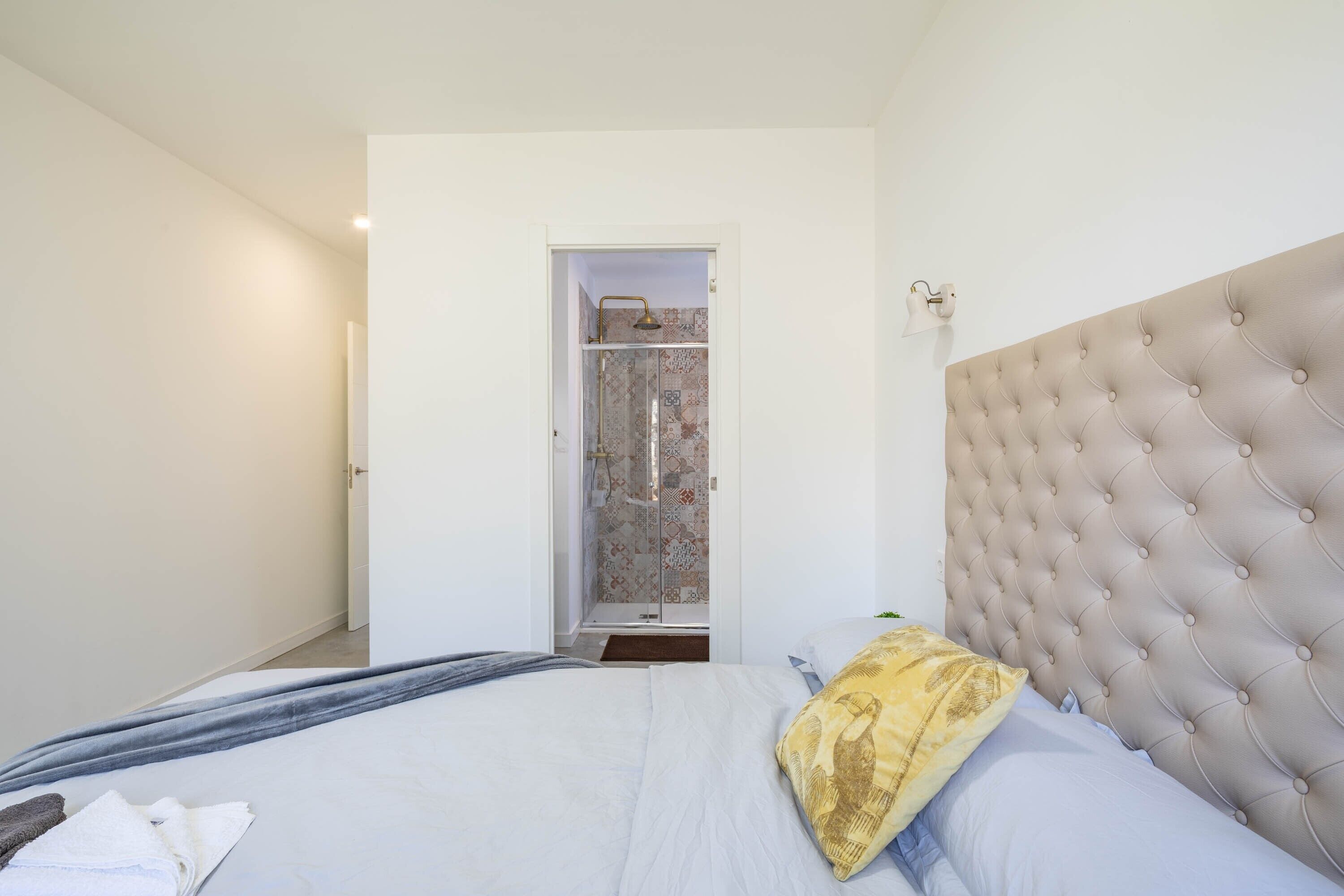 Een slaapkamer met een bed, een gestoffeerd hoofdeinde, een douche en een deur naar een badkamer.