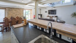 Une cuisine moderne dotée d’un grand îlot central, d’un coin repas avec des chaises en bois, d’un téléviseur à écran plat et d’un mur en pierre.