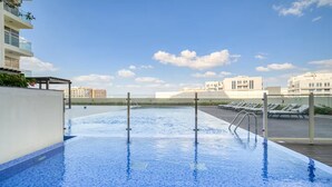 Ein Dachpool mit klarem, blauem Wasser, einer Glasbrüstung und Blick auf Gebäude im Hintergrund.