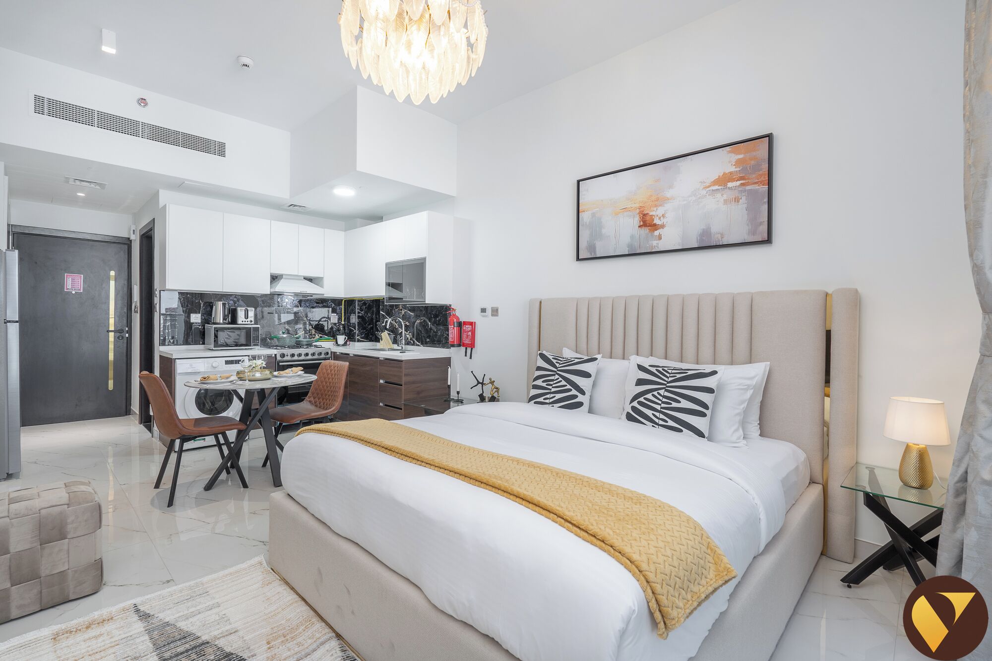 A modern hotel room with a large bed, a dining area, and a kitchen.