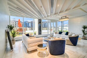 Ein geräumiges Wohnzimmer mit großen Fenstern, einem modernen Deckenstil und verschiedenen Sitzmöglichkeiten.