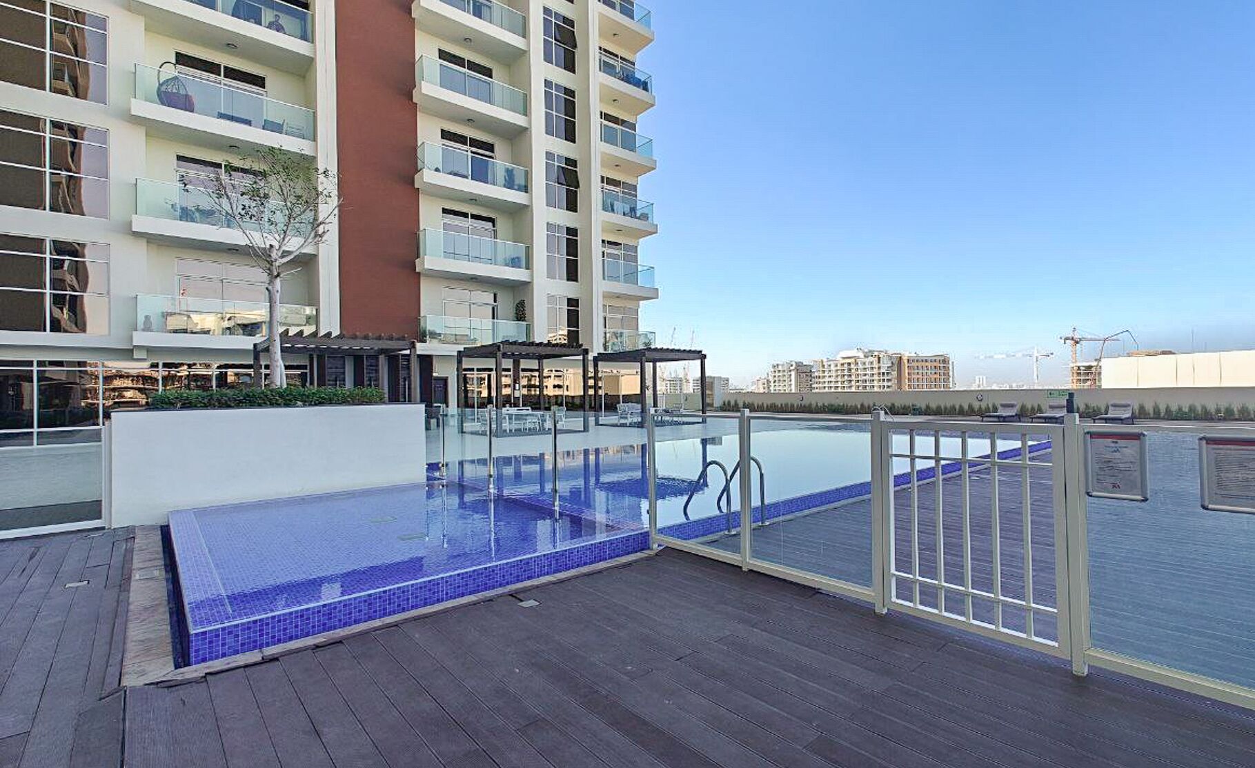 Une piscine sur le toit, dotée d’une terrasse en bois et entourée de rampes de protection en verre, offrant une vue panoramique sur la ville.
