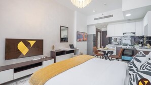 Ein modernes Hotelzimmer mit einem großen Bett, einem Schreibtisch, einem Laptop, einem Esstisch und einer Küchenzeile.