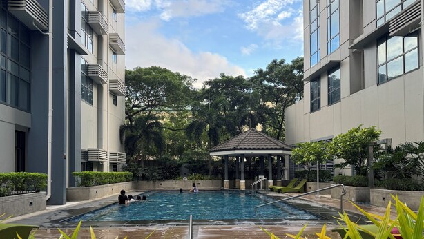 A swimming pool with a gazebo, surrounded by greenery and modern buildings. - 1BR Condo w/ Great View Near Venice Canal & BGC  (Taguig)
