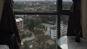 A room with a large window offering a view of a cityscape, including buildings and construction cranes. - 1BR Condo w/ Great View Near Venice Canal & BGC  (Taguig)