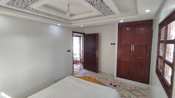 A room with a patterned ceiling, a bed with a white bedspread, a colorful rug, and wooden doors.