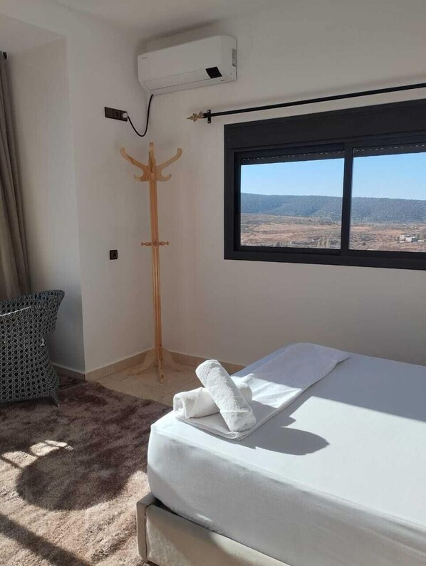 Un dormitorio con cama, ventana con vistas al paisaje, perchero y aire acondicionado.