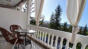 Ein Balkon mit Tisch und Stühlen, weißen Vorhängen und Blick auf Bäume und Berge.