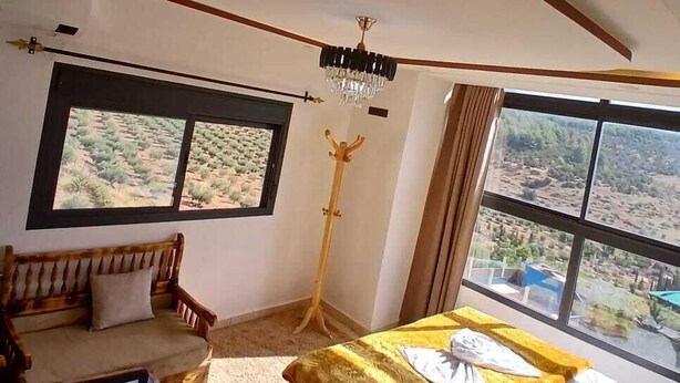Ein Schlafzimmer mit Bett, einer Couch, einer Stehlampe und Blick auf die Wüste durch große Fenster.