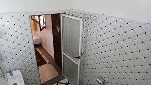 Ein kleines Badezimmer mit Fliesenboden, Toilette, Waschbecken und Duschbereich.