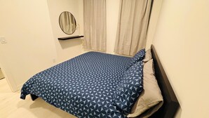 Un dormitorio con cama, mesita de noche, espejo y ventana con cortinas.